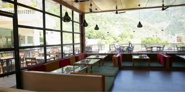 Large windows, pendant lights and lounge seating in a Rishikesh café overlooking green hills